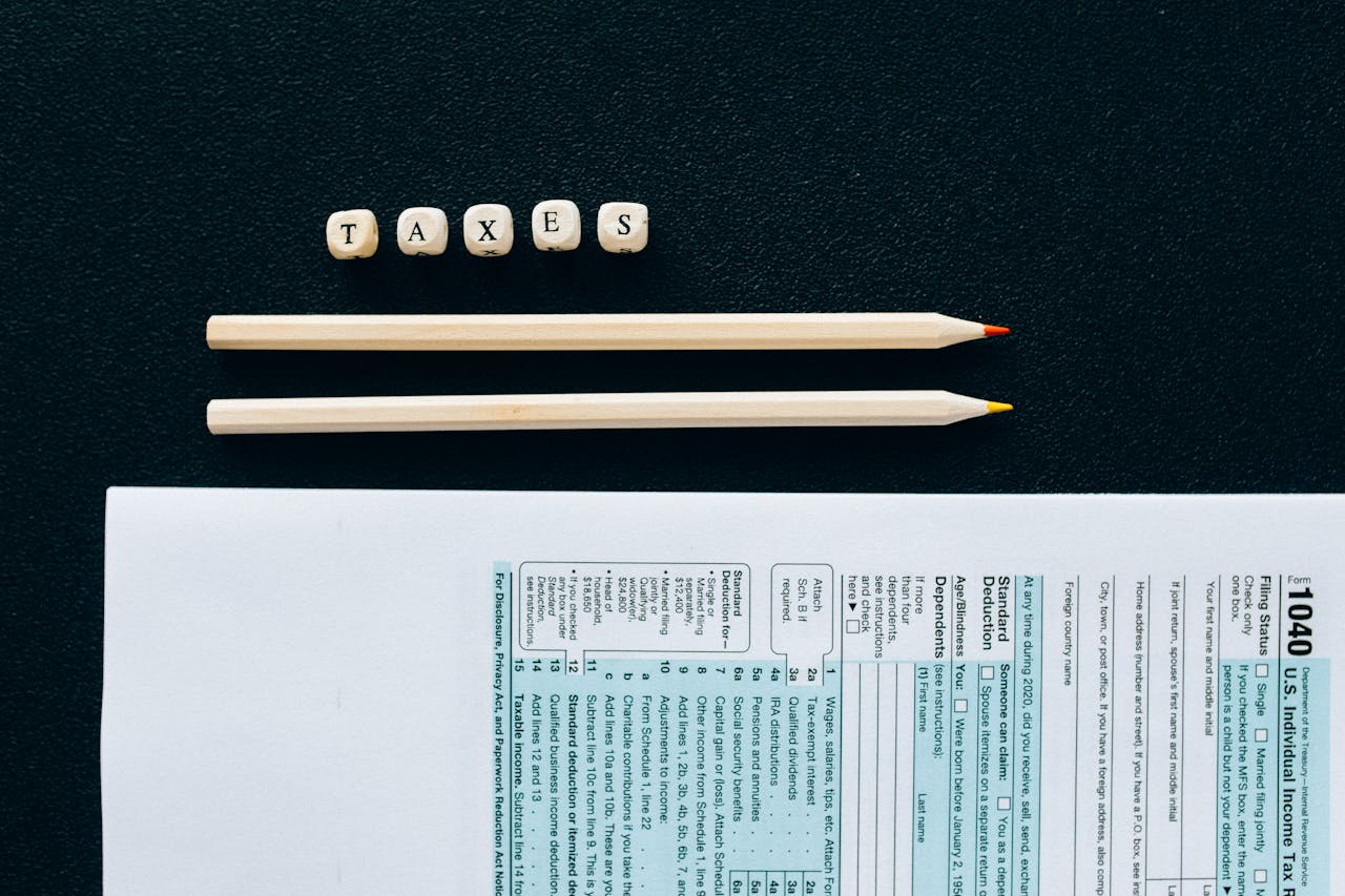 Flat lay of 1040 tax form with pencils and TAXES blocks on black background.