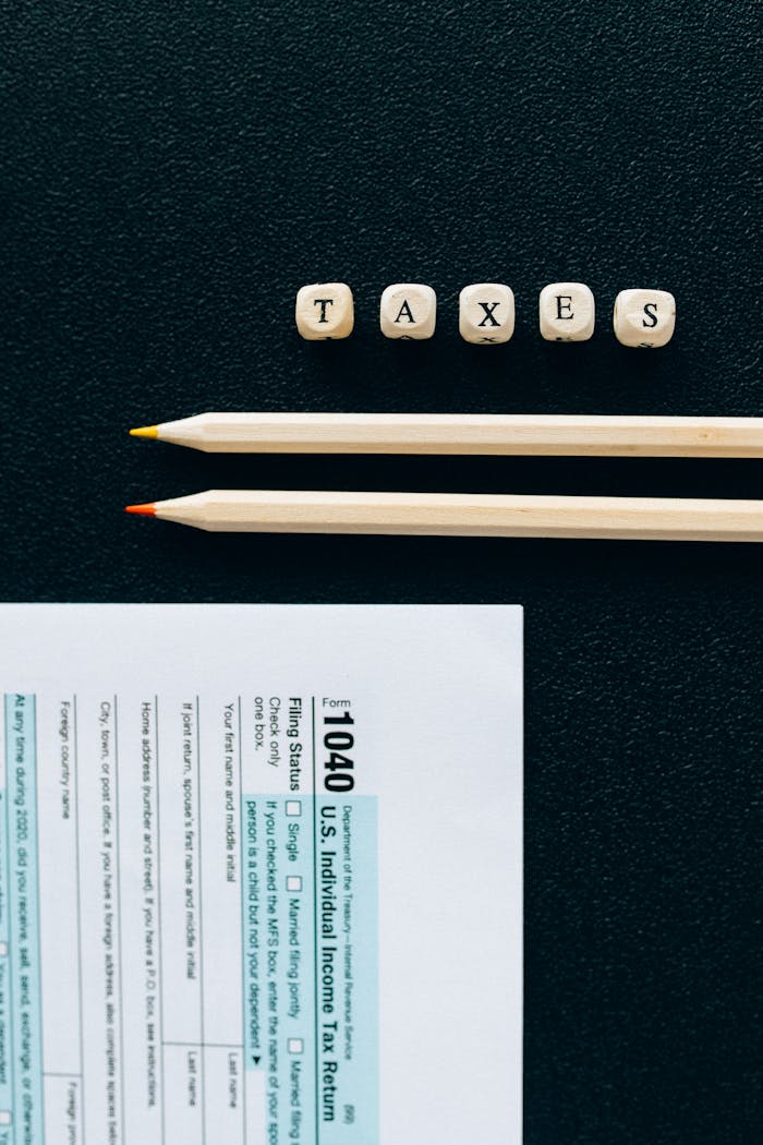 Wooden pencils and 1040 tax form on black background with tiles spelling TAXES.